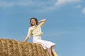 Pretty young woman sitting on haystack, countryside on blue background. Portrait of girl on high haystack