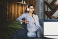 Pretty young woman sitting on sofa and listening to music on smartphone. Girl in earphones streaming songs online in social