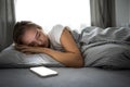Pretty, young woman sleeping in her bed with her cell phone close to her. Royalty Free Stock Photo