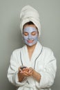 Pretty young woman spa model in blue cosmetic face mask holding organic blueberries. Facial treatment and skin care concept Royalty Free Stock Photo