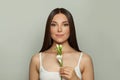 Pretty young woman spa model with clear skin smiling holding flower. Skincare, wellness and facial treatment concept