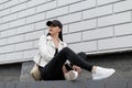 Pretty young woman in a stylish leather jacket in a t-shirt in black jeans in white sneakers in a trendy baseball cap