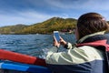 Pretty young woman taking photo on smartphone sailing lake Baikal on boat