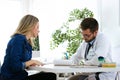 Pretty young woman talking with handsome young doctor about her health in the consultation. Royalty Free Stock Photo