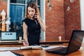 Pretty young woman talking on phone counting using a calculator working at office standing at desk Royalty Free Stock Photo