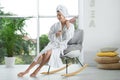 Pretty young woman with towel on head  in rocking chair near window indoors Royalty Free Stock Photo
