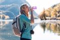 Pretty young woman traveler with backpack drinking water while standing in front of lake Royalty Free Stock Photo