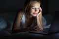 Pretty, young woman using her laptop computer in bed Royalty Free Stock Photo