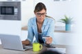 Pretty young woman using her laptpo for shopping online and paying with credit card while sitting in the kitchen at home Royalty Free Stock Photo