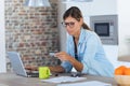 Pretty young woman using her laptpo for shopping online and paying with credit card while sitting in the kitchen at home Royalty Free Stock Photo