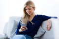 Pretty young woman using her mobile phone while sitting on sofa at home. Royalty Free Stock Photo