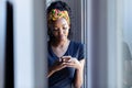 Pretty young woman using her mobile phone while standing next to the window at home Royalty Free Stock Photo