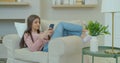 A pretty young woman using her smartphone on the couch, texting while relaxing.