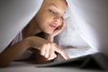 Pretty, young woman using her tablet computer in bed Royalty Free Stock Photo