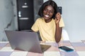 Pretty young african woman using laptop and holding credit card in kitchen Royalty Free Stock Photo