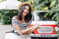 Pretty young woman with wavy brown hair posing beside red car. Outdoor portrait of joyful girl in s Royalty Free Stock Photo