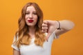 Pretty young woman with wavy redhead, wearing white t shirt showing thumb down. Dislike, failure gestures concept Royalty Free Stock Photo