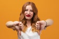 Pretty young woman with wavy redhead, wearing white t shirt showing thumb down. Dislike, failure gestures concept Royalty Free Stock Photo