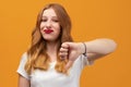Pretty young woman with wavy redhead, wearing white t-shirt showing thumb down. Dislike, failure gestures concept Royalty Free Stock Photo