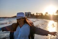 Pretty young woman in a white hat and blue jacket is spinning and having fun on the beach, at sunset Royalty Free Stock Photo