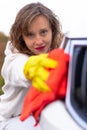 A pretty young woman in a white hoodie and yellow rubber gloves wipes the headlights of a car with a bright red rag on a warm autu Royalty Free Stock Photo