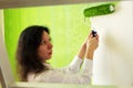 Pretty young woman in a white shirt is carefully painting green interior wall with roller in a new home Royalty Free Stock Photo