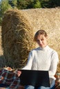 Woman in a white sweater on the background of a haystack with a laptop in her hands sits on the ground Royalty Free Stock Photo