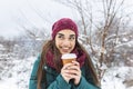 Pretty young woman in winter outfit holding disposable cup filled with hot coffee or tea. Girl holding mug of hot beverage in her