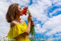 Pretty young woman in a yellow dress sniffs flowers outdoors in the countryside. Happiness and freedom concept Royalty Free Stock Photo