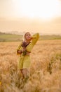 Young woman in yellow among rural field with golden oat field on sunset background Royalty Free Stock Photo