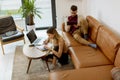 Young woman using laptop and young man using digital tablet while sitting on sofa at home Royalty Free Stock Photo