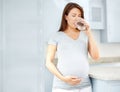 Preventing complications. Young pregnant woman drinking a glass of water in her kitchen while holding her belly. Royalty Free Stock Photo