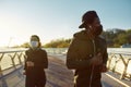 Preventing virus. Young african man and woman in medical masks running on the bridge during a pandemic. Sport and Royalty Free Stock Photo