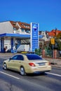 Price board of an Aral Group gas station with extremely high prices and a blurred taxi in the foreground