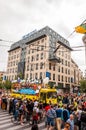 Pride parade event in action. Crowd of watchers surrounding yellow open top bus decorated with white balloons full of