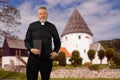A priest in a black shirt stands in front of a small white round church on the island of Bornholm. Royalty Free Stock Photo