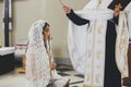 Priest blessing with holy water stylish bride in kerchief at altar during holy matrimony in church. Wedding ceremony in cathedral Royalty Free Stock Photo