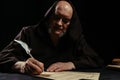 priest in dark hooded cassock writing