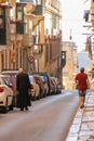 Priest dressed black attire and man in red t-shirt walk on Valletta street towards Grand Harbour