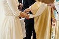 Priest holding hands of stylish bride and elegant groom at catholic wedding ceremony at church