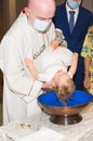 Priest with mask, Covid-19, celebrates the baptism of a girl in the baptismal font