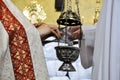 The priest places incense inside the thurible that the acolyte holds with his hands and, in the background, the Blessed Sacrament