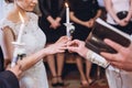 Priest putting on wedding ring on beautiful bride in wedding dress, gorgeous bride and groom holding candles in church