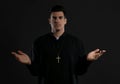 Priest wearing cassock with clerical collar on black background