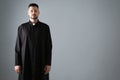 Priest wearing cassock with clerical collar on grey, space for text