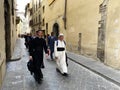 Priest wearing a white cassock and the seminarians in black dress walking in the streets of Florence