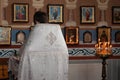 Priest in white cassock conduct service in front of pulpit, icons and candles in orthodox church