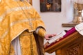 The priest in a yellow vestment with a cross on his chest holding a hand page of the Bible