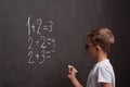 Primary education. Rear view of a schoolboy solves a mathematical example on a blackboard in a math class