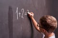Primary education. Rear view of a schoolboy solves a mathematical example on a blackboard in a math class Royalty Free Stock Photo